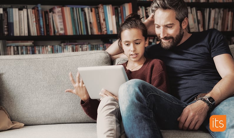 Père et fille assis dans le canapé de leur salon tout en regardant une tablette ensemble.